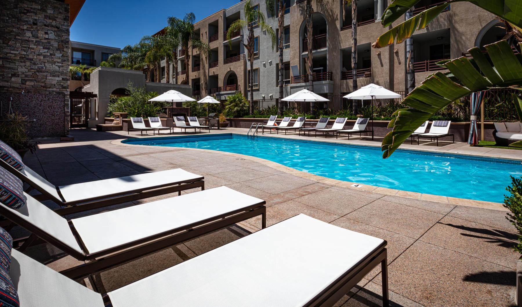 a pool with lounge chairs and umbrellas by a building